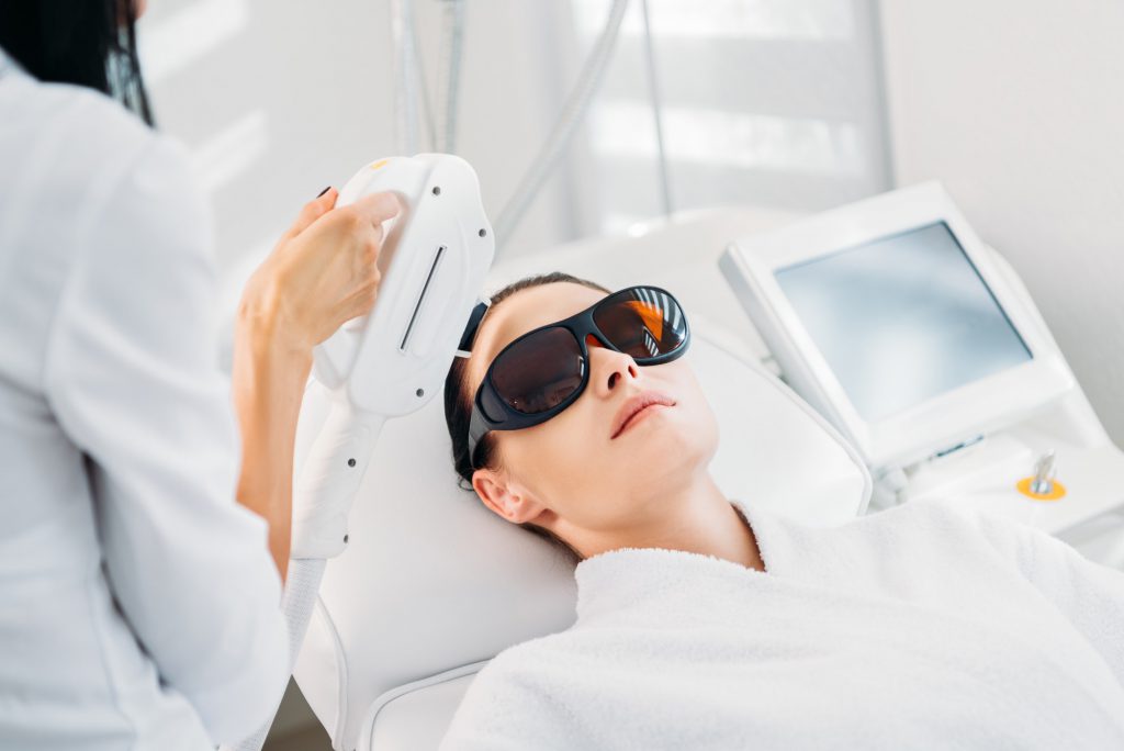woman in protective eyeglasses getting laser hair removal made by cosmetologist in spa salon